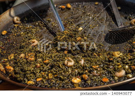Close-up of black seafood paella with rice, shrimp and mussels cooked in large pan. Traditional Spanish arroz negro served at outdoor food event 140943077