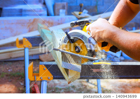 Handyman cuts piece of wood with circular saw dust flies as saw moves. 140943699