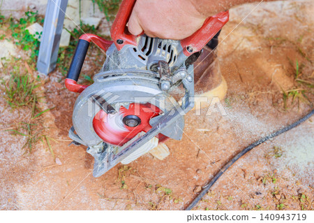 Contractor operates circular saw to cut through surface, with dust flying in air, tools nearby. Contractor operates circular saw to cut through surface, with dust flying in air, tools nearby. 140943719