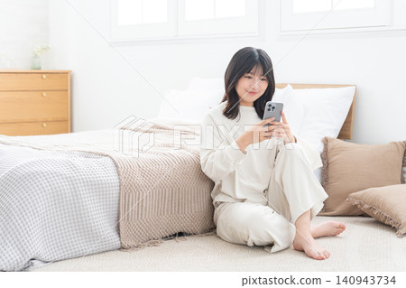 Woman using smartphone in bedroom Woman using smartphone in bedroom 140943734