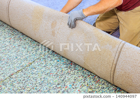 Worker rolls up carpet to prepare for installation cleaning in bright room with light floor. Worker rolls up carpet to prepare for installation cleaning in bright room with light floor. 140944097