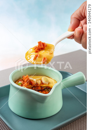 Close up of porcelain spoon holding steamed egg custard with chopped ham and scallions Close up of porcelain spoon holding steamed egg custard with chopped ham and scallions 140944179