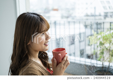 A young woman drinking coffee by the window on a rainy day. A young woman drinking coffee by the window on a rainy day. 140944519