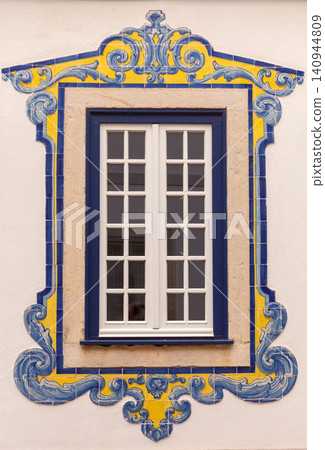 Close-up of an ornate blue and yellow azulejo tile panel framing a window on a historic Portuguese house in Cascais, Portugal. Close-up of an ornate blue and yellow azulejo tile panel framing a window on a historic Portuguese house in Cascais, Portugal. 140944809