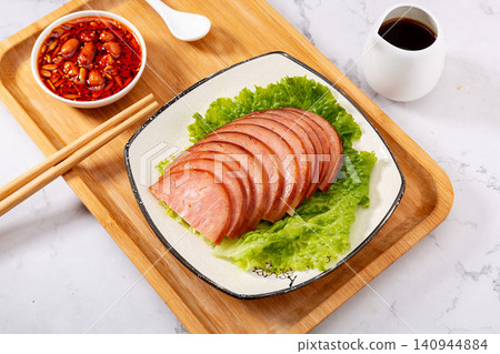dipping sliced Chinese pine nut pork sausage into spicy chili oil, savory cold appetizer preparation dipping sliced Chinese pine nut pork sausage into spicy chili oil, savory cold appetizer preparation 140944884