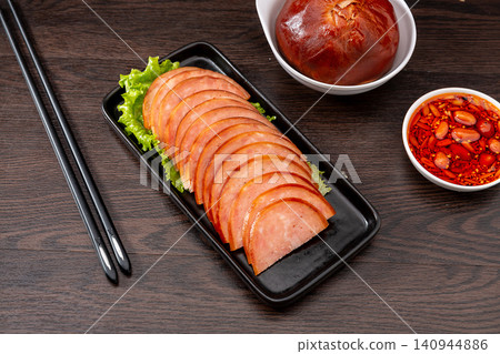 dipping sliced Chinese pine nut pork sausage into spicy chili oil, savory cold appetizer preparation dipping sliced Chinese pine nut pork sausage into spicy chili oil, savory cold appetizer preparation 140944886