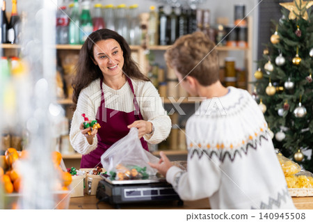 Teenage boy buys candies in supermarket. Positive female seller weighs candies on scales Teenage boy buys candies in supermarket. Positive female seller weighs candies on scales 140945508