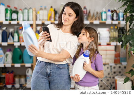 Mother and daughter checking expiration date of detergent using her smartphone in supermarket Mother and daughter checking expiration date of detergent using her smartphone in supermarket 140945558
