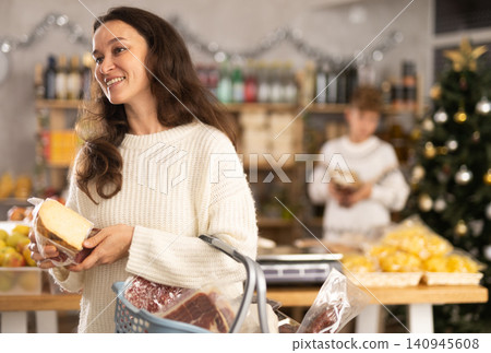 Portrait of female shopper with cart cheese and meat choosing food and wine for Christmas celebration in grocery department of shop Portrait of female shopper with cart cheese and meat choosing food and wine for Christmas celebration in grocery department of shop 140945608