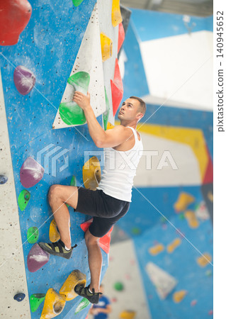 Young man climbing on artificial rock wall in rock-climbing gym Young man climbing on artificial rock wall in rock-climbing gym 140945652