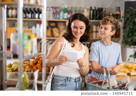 In store near snack display case, mom and son stand with paper list, recall planned products In store near snack display case, mom and son stand with paper list, recall planned products 140945715