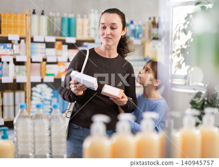 Woman with schoolgirl daughter are busy choosing tablet box at pharmacy Woman with schoolgirl daughter are busy choosing tablet box at pharmacy 140945757