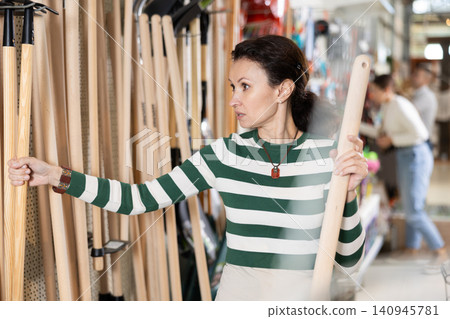 Amateur gardener woman selects necessary items tools for her hobby in greenhouse flower-bed 140945781