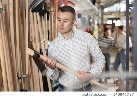 Amateur gardener man selects necessary items tools for her hobby in greenhouse flower-bed 140945787
