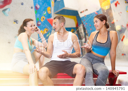 Young man and two women talking merrily sitting in climbing hangar Young man and two women talking merrily sitting in climbing hangar 140945791