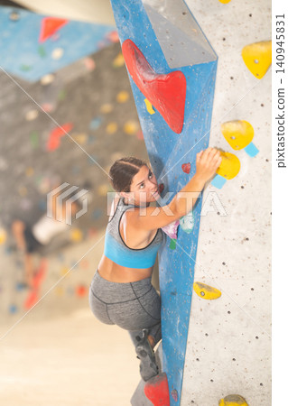 Young girl climbing on artificial rock wall in rock-climbing gym Young girl climbing on artificial rock wall in rock-climbing gym 140945831