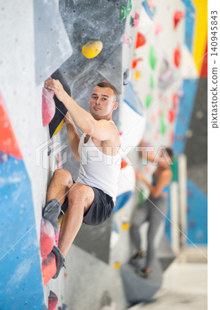 Young man climbing on artificial rock wall in rock-climbing gym Young man climbing on artificial rock wall in rock-climbing gym 140945843