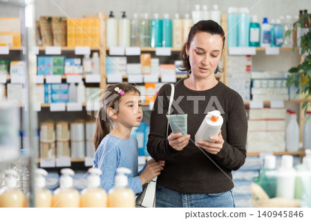 Woman with daughter choosing cream in pharmacy Woman with daughter choosing cream in pharmacy 140945846