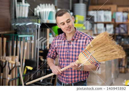Young man choosing broom in household store Young man choosing broom in household store 140945892