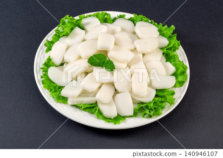 Raw white rice cake slices arranged with fresh green lettuce leaves. Raw white rice cake slices arranged with fresh green lettuce leaves. 140946107
