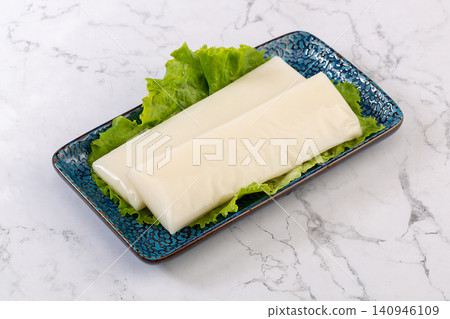 Raw white rice cake slices arranged with fresh green lettuce leaves. Raw white rice cake slices arranged with fresh green lettuce leaves. 140946109