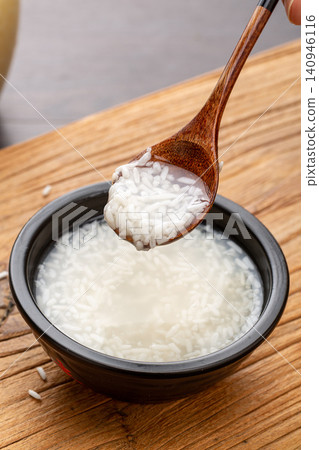 close-up of a wooden spoon scooping fermented sweet rice wine above a black bowl on a wooden board. close-up of a wooden spoon scooping fermented sweet rice wine above a black bowl on a wooden board. 140946116