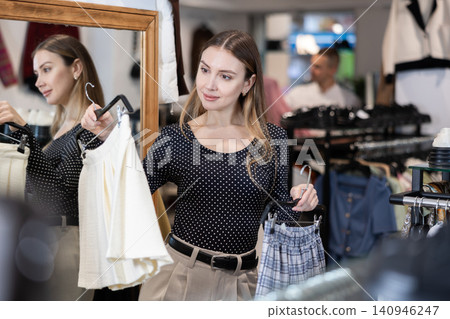 Girl stopped near showcase with outerwear, holds skirt hanger in hands and examines product 140946247