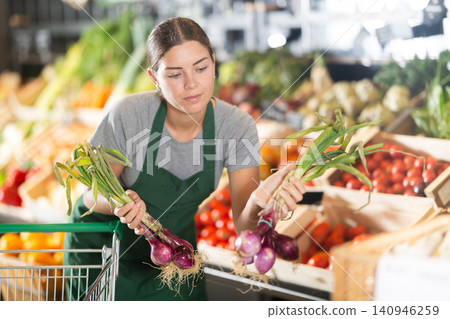 Female shop assistant displaying bunches of fresh purple onions Female shop assistant displaying bunches of fresh purple onions 140946259