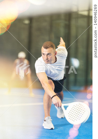 Male players playing padel in a padel court indoor behind net Male players playing padel in a padel court indoor behind net 140946269