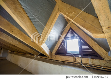 Attic of a building with wooden beams of a roof structure and a small window. Attic of a building with wooden beams of a roof structure and a small window. 140946287