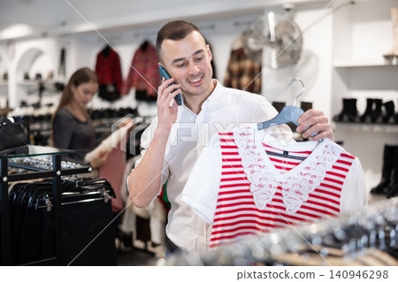 Young man chooses blouse and talks on phone Young man chooses blouse and talks on phone 140946298