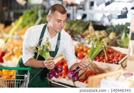 Man supermarket worker with onion in hands examines product 140946345
