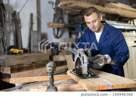 Young man saws oak plank in workshop Young man saws oak plank in workshop 140946366