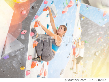 Young girl climbing on artificial rock wall in rock-climbing gym Young girl climbing on artificial rock wall in rock-climbing gym 140946464