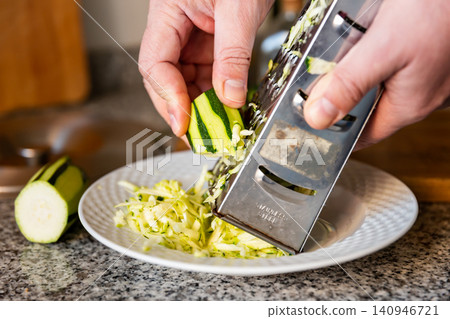 Mens hands hold piece of ripe zucchini and chop vegetables with grater Mens hands hold piece of ripe zucchini and chop vegetables with grater 140946721