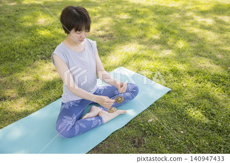 一名女子在戶外瑜珈時使用鈴鐺來集中註意力。 一名女子在戶外瑜珈時使用鈴鐺來集中註意力。 140947433