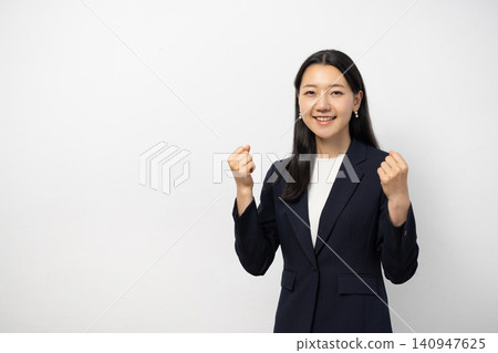 A young Japanese businesswoman strikes a triumphant pose in front of a white wall and smiles at the camera. A young Japanese businesswoman strikes a triumphant pose in front of a white wall and smiles at the camera. 140947625
