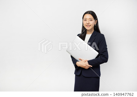A young Japanese businesswoman smiles at the camera, holding a laptop, in front of a white wall. A young Japanese businesswoman smiles at the camera, holding a laptop, in front of a white wall. 140947762