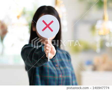 一位年輕女子舉著一塊寫有「X」的牌子。 一位年輕女子舉著一塊寫有「X」的牌子。 140947774