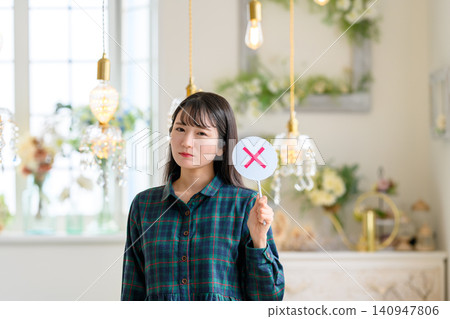 A woman with a serious expression holding a sign marked with an "X". A woman with a serious expression holding a sign marked with an "X". 140947806