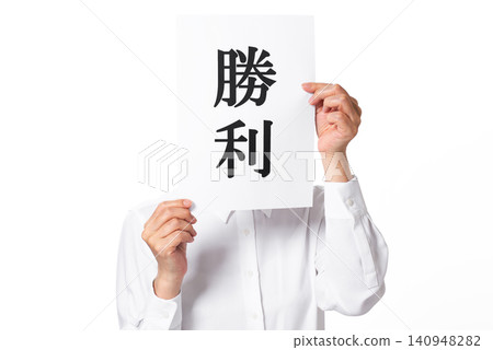 A person in a white shirt holding a piece of paper with the word "Victory" written on it in both hands. A person in a white shirt holding a piece of paper with the word "Victory" written on it in both hands. 140948282