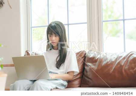 坐在沙發上並使用個人電腦的女孩 坐在沙發上並使用個人電腦的女孩 140948454