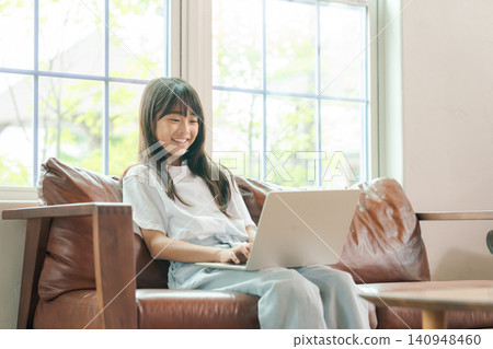 A girl who sits on a sofa and uses a personal computer A girl who sits on a sofa and uses a personal computer 140948460