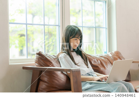 A girl who sits on a sofa and uses a personal computer A girl who sits on a sofa and uses a personal computer 140948461