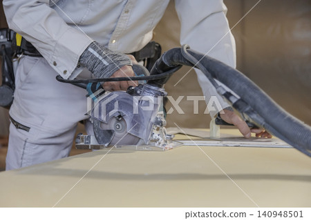 A side view of a worker cutting a building material panel with a rotating circular saw blade. A side view of a worker cutting a building material panel with a rotating circular saw blade. 140948501