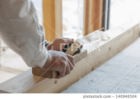 A craftsman's hands planing a piece of lumber in the light from a window, finishing the surface of the wood. 140948504