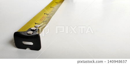 Close-up photo of a yellow tape measure with metric and imperial scales on a white background. Close-up photo of a yellow tape measure with metric and imperial scales on a white background. 140948637