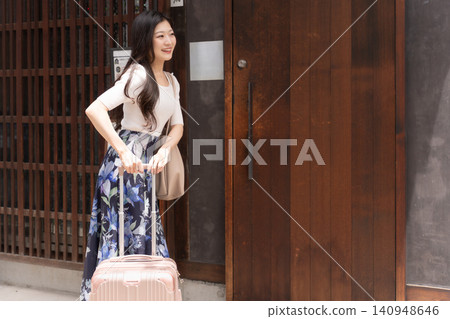A young woman with a suitcase arrives at a guesthouse with a traditional Japanese house style and checks in. A young woman with a suitcase arrives at a guesthouse with a traditional Japanese house style and checks in. 140948646