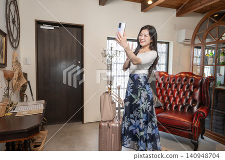A young woman with a suitcase arrives at a guesthouse with a traditional Japanese house style and takes a selfie with her smartphone. A young woman with a suitcase arrives at a guesthouse with a traditional Japanese house style and takes a selfie with her smartphone. 140948704