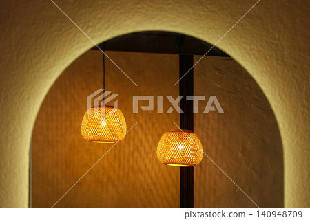 Woven Straw Lampshade with Glowing Light Bulb Creating Shadows at Night 140948709